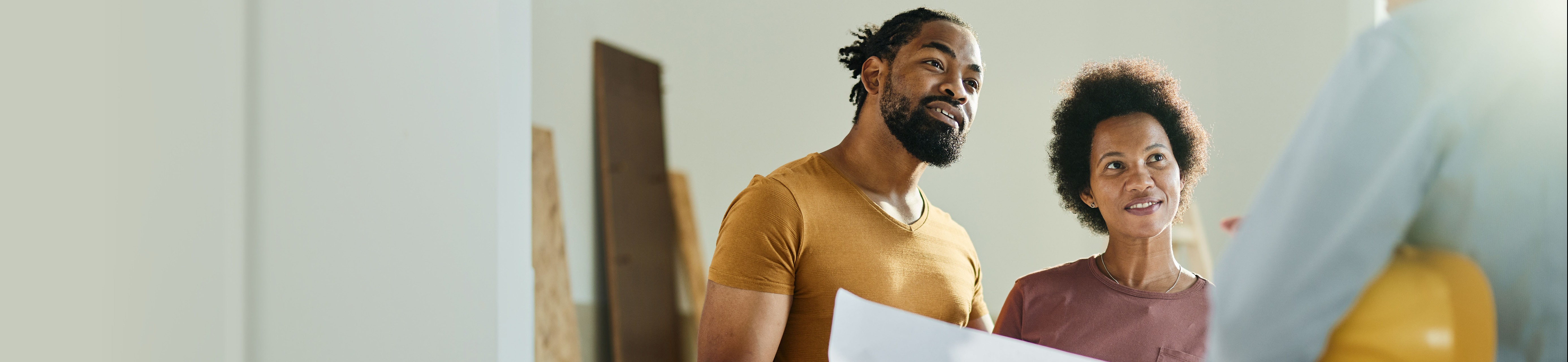 young couple holding blueprint discussing changes with contractor